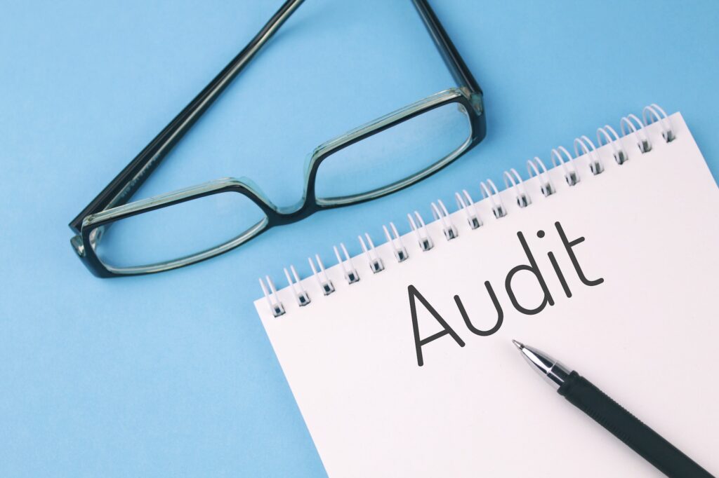 Reading glasses and blank with word AUDIT on a blue background