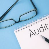 Reading glasses and blank with word AUDIT on a blue background